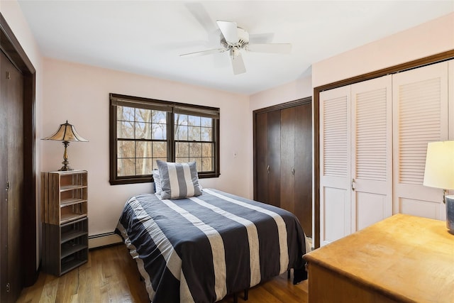 bedroom featuring ceiling fan, a baseboard heating unit, two closets, and wood finished floors