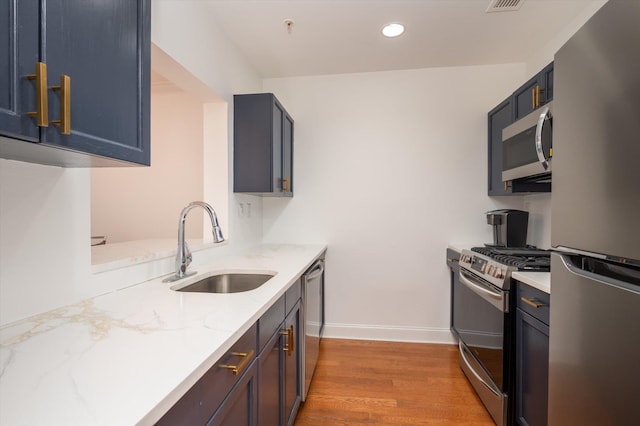 kitchen with appliances with stainless steel finishes, light wood-style floors, a sink, light stone countertops, and baseboards