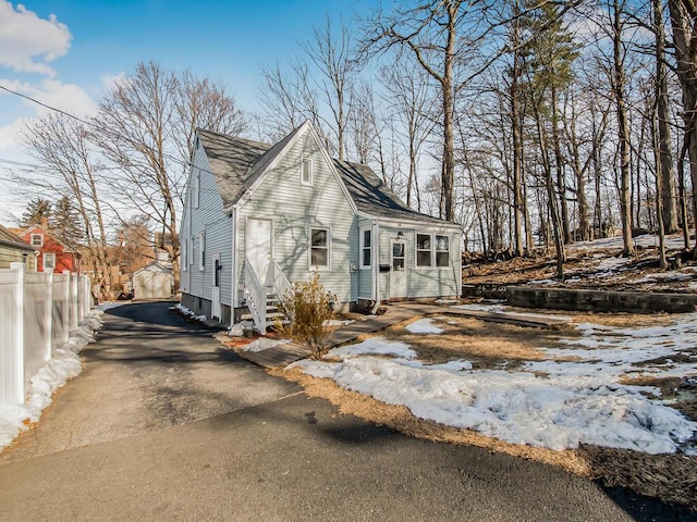 view of snowy exterior featuring entry steps, driveway, a shingled roof, and fence