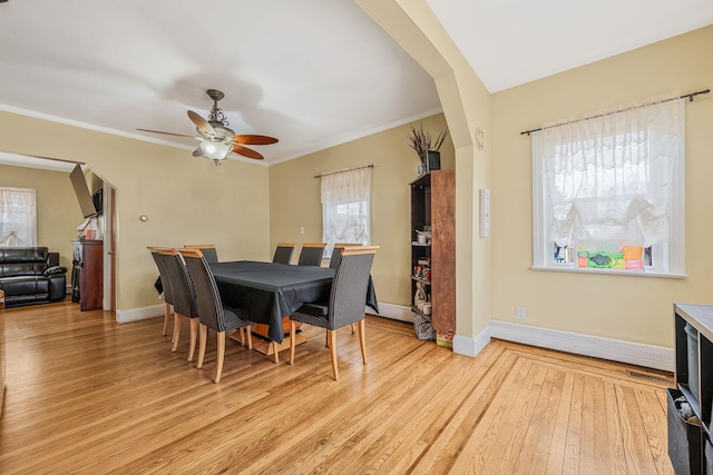 dining area featuring arched walkways, a baseboard radiator, baseboards, light wood-type flooring, and crown molding