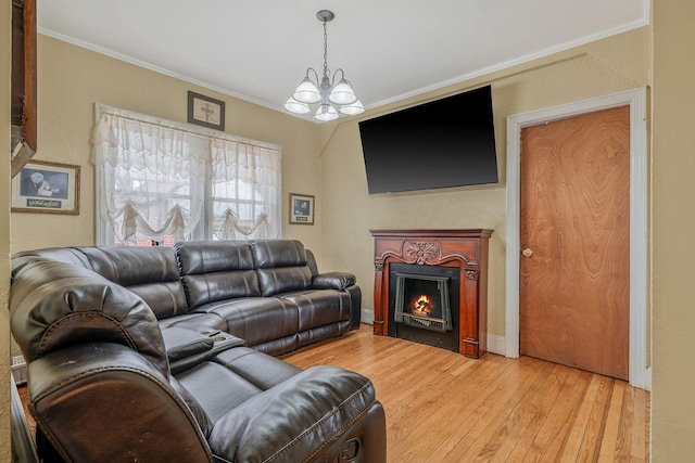 living room with ornamental molding, a warm lit fireplace, a chandelier, and light wood finished floors