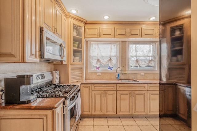 kitchen featuring light tile patterned floors, a sink, appliances with stainless steel finishes, tasteful backsplash, and glass insert cabinets