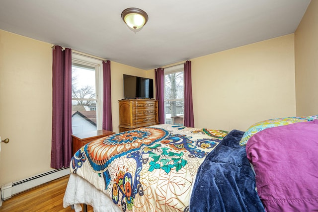 bedroom with a baseboard heating unit and light wood-style floors