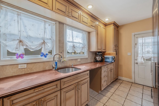 kitchen featuring dark countertops, backsplash, light tile patterned flooring, a sink, and baseboards