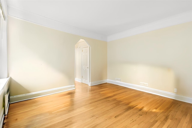 unfurnished room with ornamental molding, arched walkways, light wood-style flooring, and baseboards