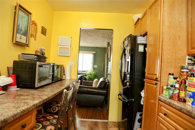 kitchen featuring dark wood-style floors, brown cabinetry, and freestanding refrigerator