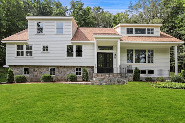 view of front facade with stone siding, a front lawn, and roof with shingles