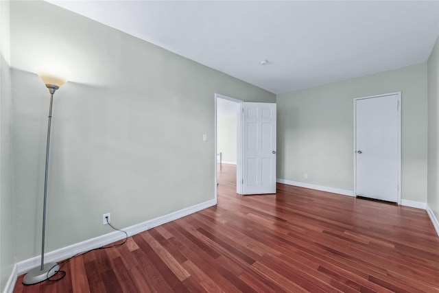 unfurnished bedroom featuring lofted ceiling, baseboards, and dark wood-type flooring