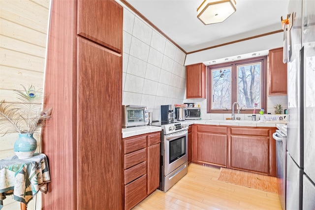 kitchen with tile countertops, a sink, light wood-type flooring, stainless steel electric stove, and crown molding