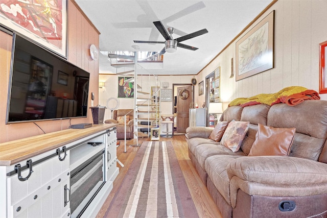 living area with ornamental molding, ceiling fan, light wood finished floors, and stairs