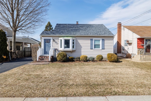 bungalow-style house with a front lawn, a shingled roof, and fence