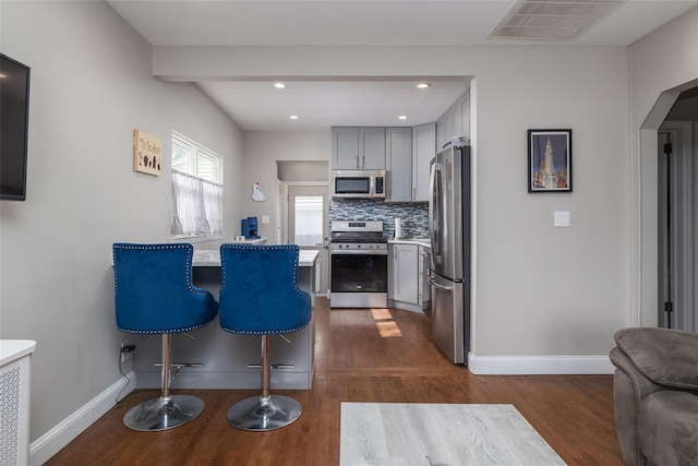 kitchen with a breakfast bar area, tasteful backsplash, visible vents, gray cabinetry, and appliances with stainless steel finishes