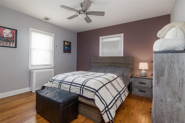 bedroom featuring ceiling fan, light wood-style flooring, visible vents, baseboards, and radiator