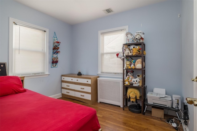 bedroom featuring wood finished floors, visible vents, and radiator