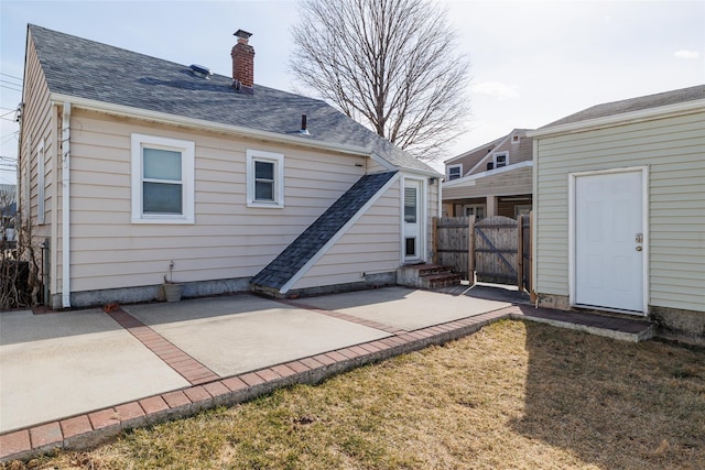 rear view of property with fence, roof with shingles, a gate, a chimney, and a patio area