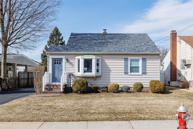 bungalow-style home featuring aphalt driveway, a wall unit AC, fence, roof with shingles, and a front yard