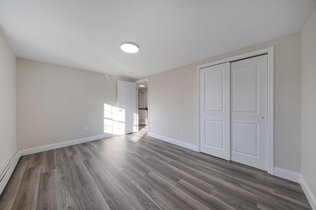 unfurnished bedroom featuring a baseboard heating unit, a closet, dark wood finished floors, and baseboards