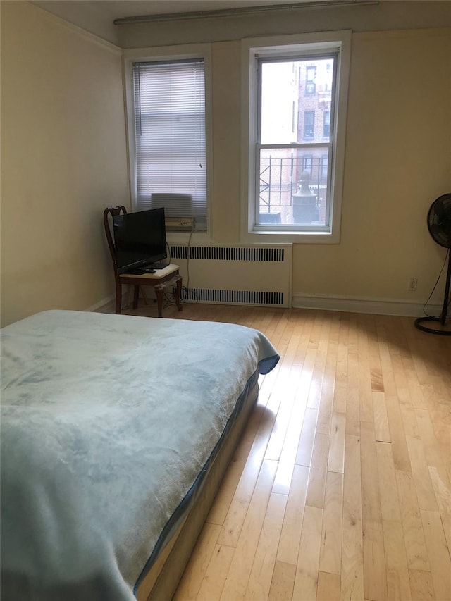 bedroom with baseboards, light wood-type flooring, and radiator