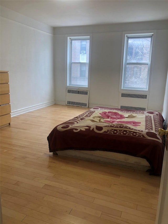 bedroom featuring radiator, light wood finished floors, multiple windows, and baseboards