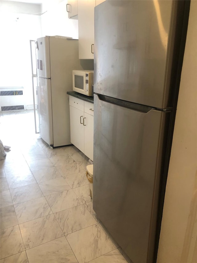 kitchen featuring white appliances, dark countertops, radiator, marble finish floor, and white cabinetry