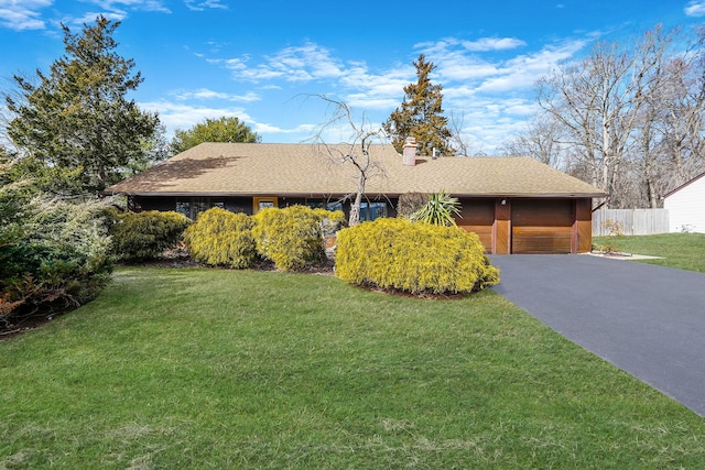 single story home with aphalt driveway, a chimney, an attached garage, fence, and a front lawn