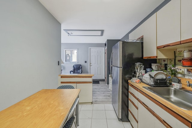 kitchen with light tile patterned flooring, a sink, wood counters, and white cabinets