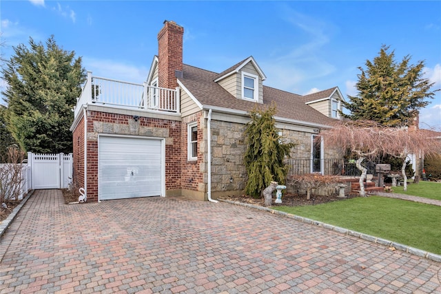 view of front facade with an attached garage, a balcony, fence, stone siding, and decorative driveway