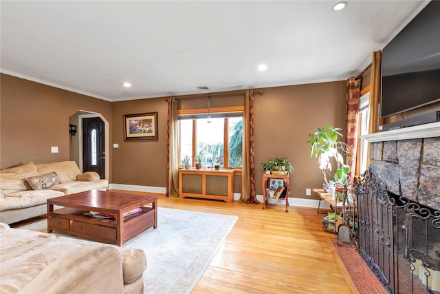 living area featuring arched walkways, baseboards, radiator heating unit, light wood-type flooring, and a fireplace