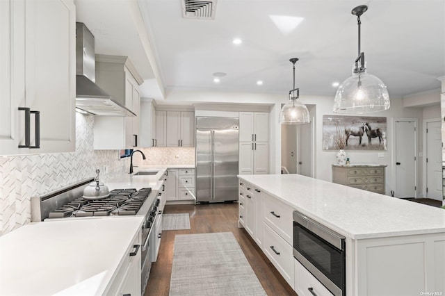 kitchen with built in appliances, a kitchen island, a sink, visible vents, and wall chimney exhaust hood