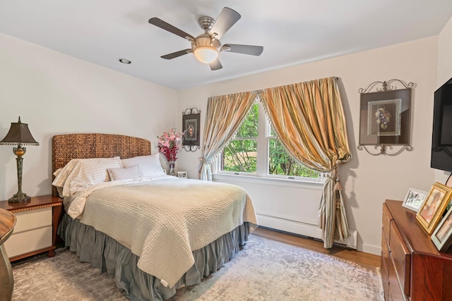 bedroom with a baseboard heating unit, wood finished floors, a ceiling fan, and baseboards