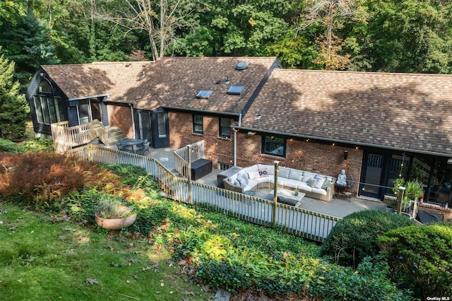 rear view of property with roof with shingles, a deck, an outdoor hangout area, and brick siding