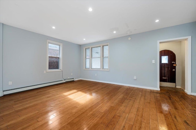 unfurnished room featuring light wood-style floors, a baseboard radiator, arched walkways, and baseboards