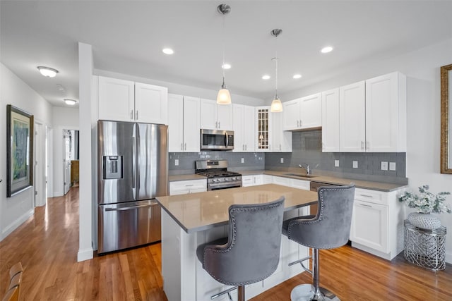 kitchen featuring stainless steel appliances, wood finished floors, a sink, a kitchen breakfast bar, and a center island