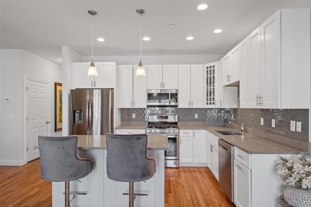 kitchen with light wood finished floors, glass insert cabinets, stainless steel appliances, a kitchen bar, and a sink