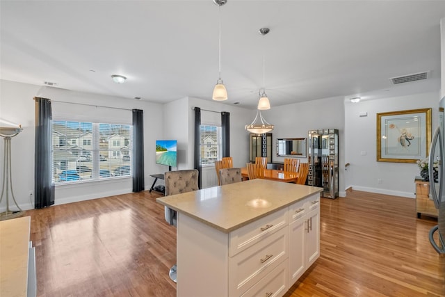 kitchen featuring a center island, decorative light fixtures, light countertops, white cabinets, and light wood-type flooring