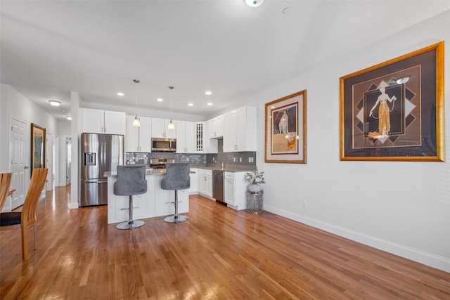 kitchen with a breakfast bar, backsplash, appliances with stainless steel finishes, white cabinets, and wood finished floors