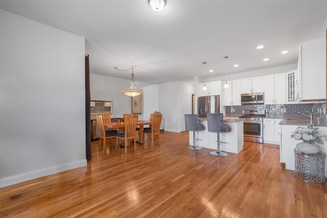 kitchen with a center island, backsplash, appliances with stainless steel finishes, light wood-type flooring, and a kitchen bar