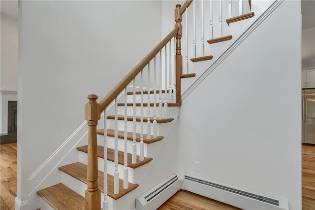 stairs featuring a baseboard radiator, baseboards, and wood finished floors