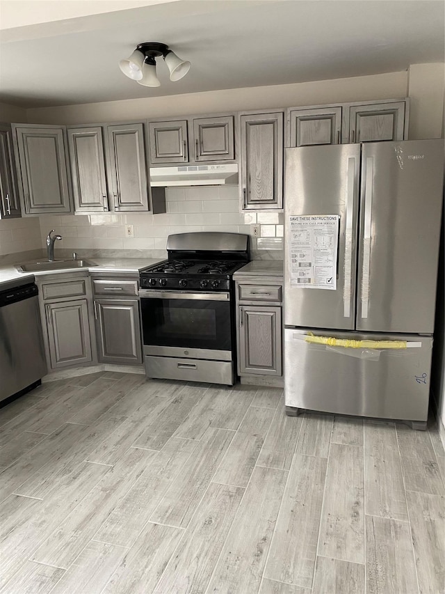 kitchen featuring under cabinet range hood, stainless steel appliances, a sink, light wood-type flooring, and backsplash