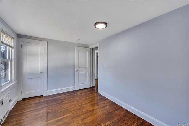 unfurnished bedroom featuring baseboards, a closet, dark wood finished floors, and radiator