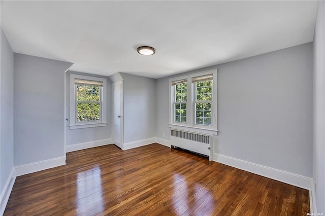 empty room featuring radiator, dark wood-style floors, and baseboards