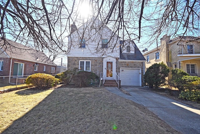 view of front of property featuring a garage, driveway, stone siding, fence, and a front yard