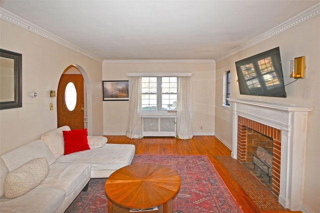 living room featuring ornamental molding, radiator heating unit, a brick fireplace, and wood finished floors