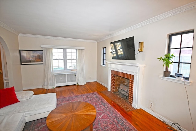 living area with a brick fireplace, radiator heating unit, arched walkways, and wood finished floors