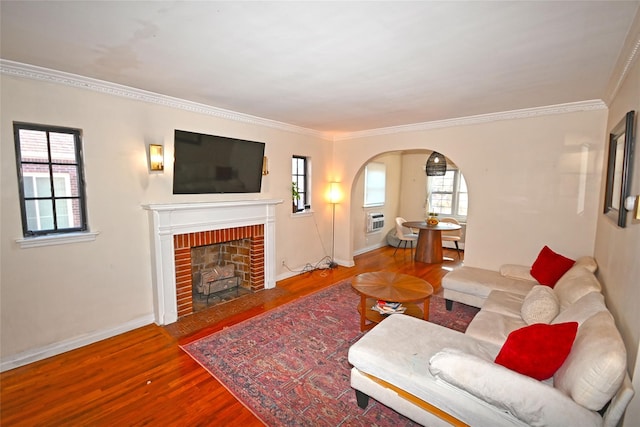 living room featuring baseboards, arched walkways, ornamental molding, wood finished floors, and a fireplace