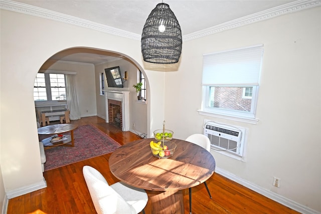 dining area featuring arched walkways, wood finished floors, ornamental molding, a brick fireplace, and a wall mounted air conditioner