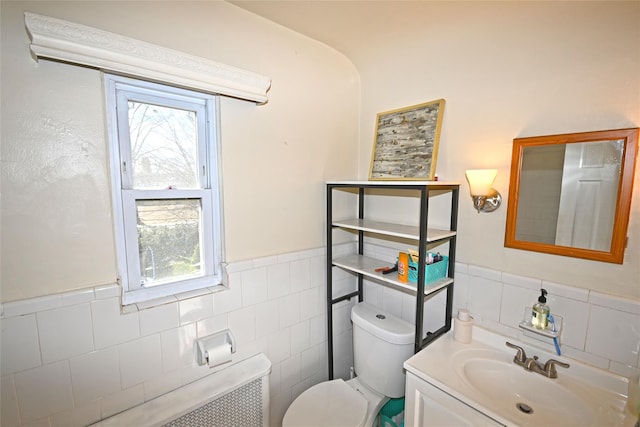 half bath with a wainscoted wall, plenty of natural light, tile walls, and toilet