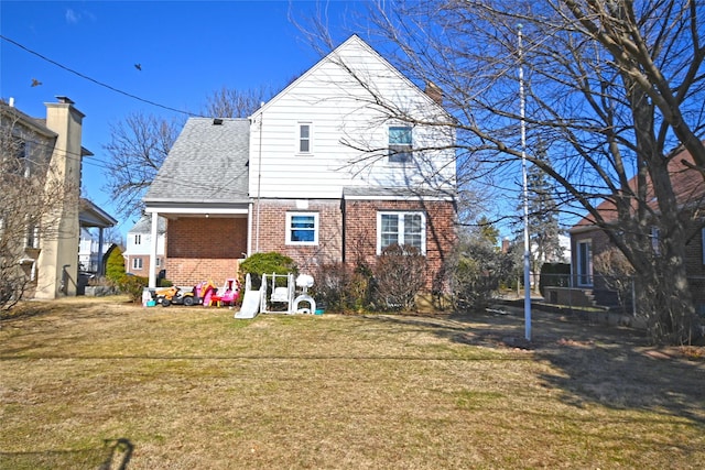 back of house featuring a yard, brick siding, and a shingled roof