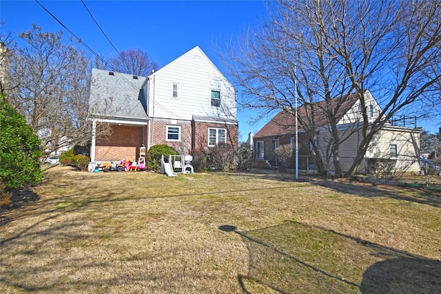 back of property featuring brick siding, a yard, and roof with shingles