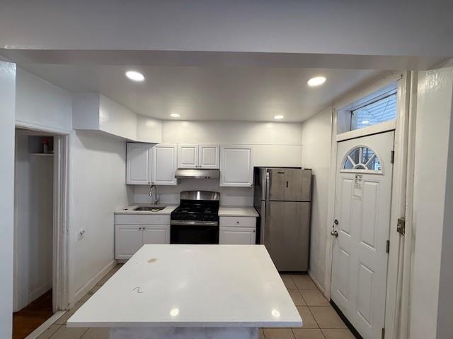 kitchen with under cabinet range hood, a sink, white cabinets, light countertops, and appliances with stainless steel finishes